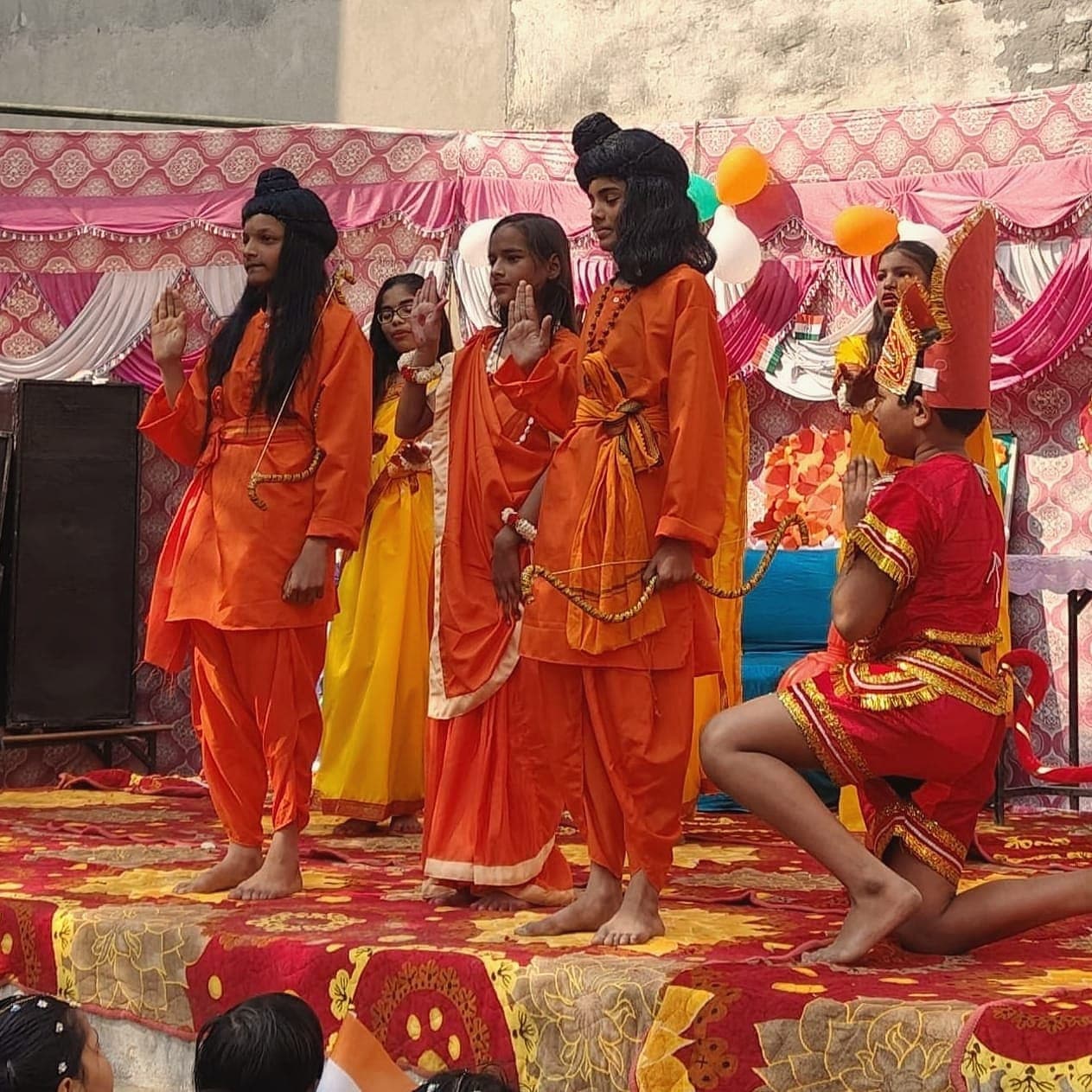 Students mid-performance in orange costumes on the annual function stage